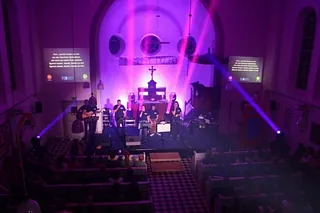 Gottesdienst mit lila Beleuchtung, Musikern und projiziertem Text.