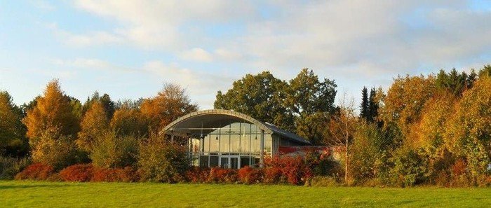 Modernes Gebäude mit geschwungenem Dach in Herbstlandschaft.