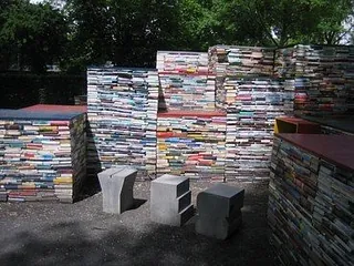 Skulptur oder Bauwerk aus gestapelten Büchern im Freien, mit Sitzgelegenheiten.