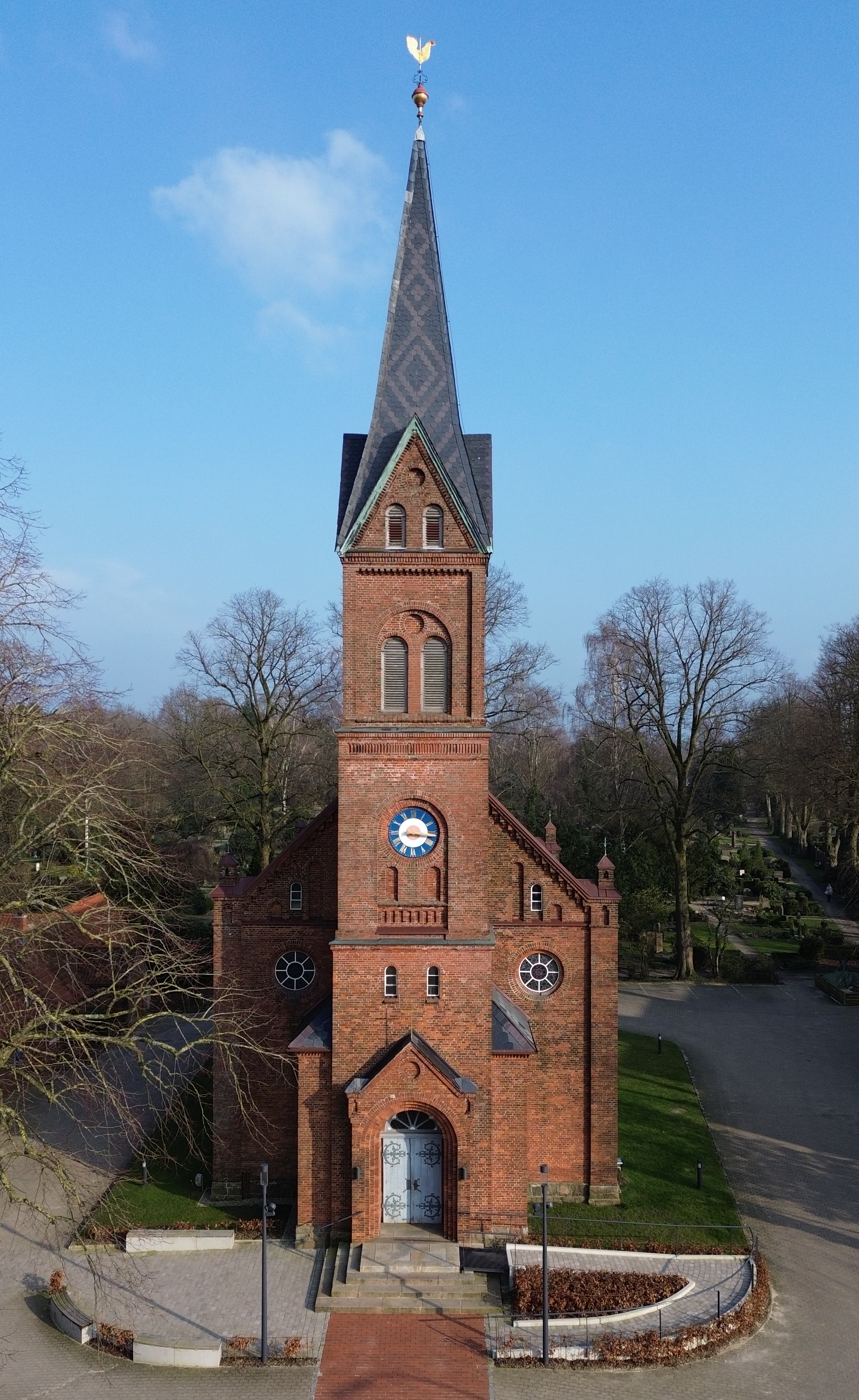 Rote Backsteinkirche mit hohem, spitzem Turm unter blauem Himmel.