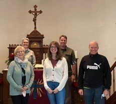 Eine Gruppe von fünf Personen steht vor einem Altar mit einem Kruzifix.