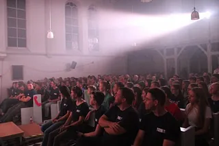 Große Menschenmenge in einer abgedunkelten Halle, durch Lichtstrahlen beleuchtet.