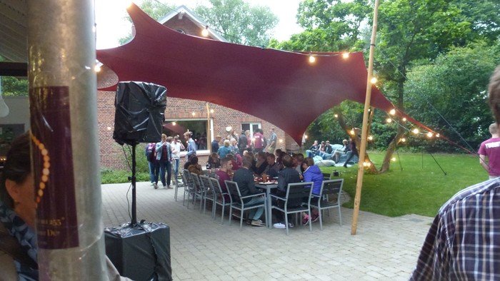 Menschen sitzen an Tischen im Freien unter einem großen, roten Tuch.