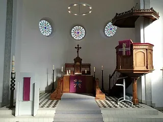 Kircheninnenraum mit Altar, Kanzel und runden Fenstern.