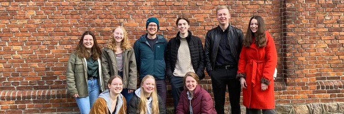 Gruppe von jungen Leuten posiert für ein Foto vor einer Backsteinmauer.