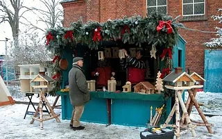 Mann an Weihnachtsmarktstand mit Holzhandwerk im Schneefall.