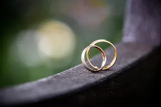 Zwei goldene Eheringe liegen auf einem schwarzen Geländer.