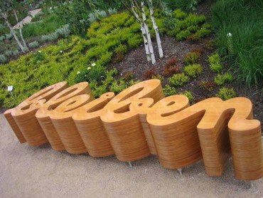 Holzskulptur mit dem Wort „Bleiben“ in einem Garten.